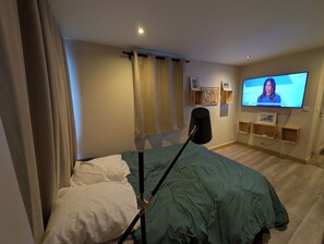 Une chambre à coucher comprenant un lit, une télévision, une lampe et des étagères fixées au mur.