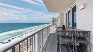 A balcony with a view of the beach and ocean, a table with chairs, and a window. - 🌞🩴Gulf-Front 3BR | Great Amenities + Steps to Beach | Summerwind West 1403 (Navarre Beach)