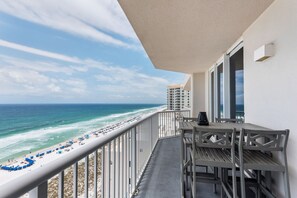 Ein Balkon mit Blick auf Strand und Meer, inklusive Tisch und Stühlen sowie ein Fenster.