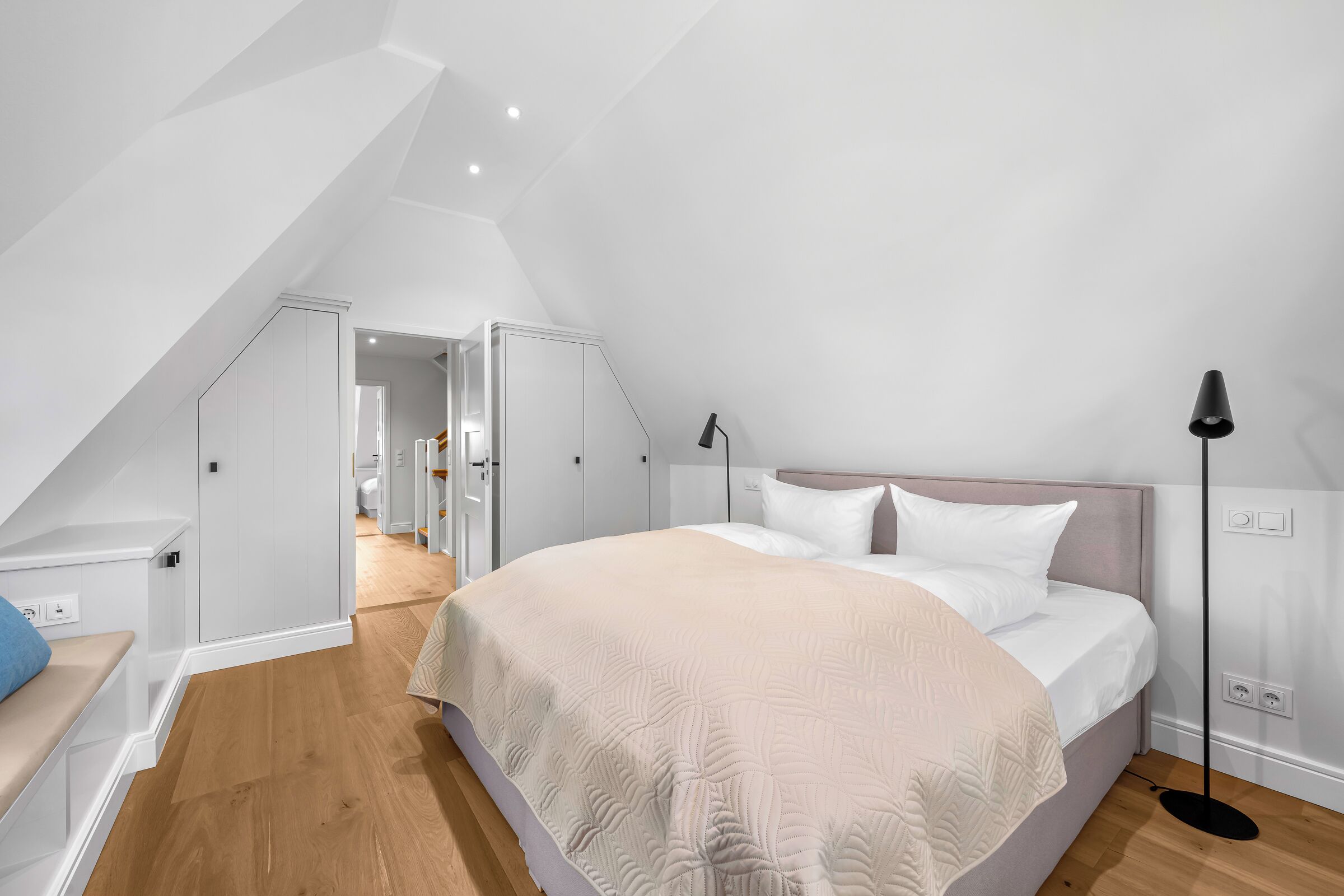 A bedroom with a large bed, a nightstand, a lamp, and a view of a hallway.
