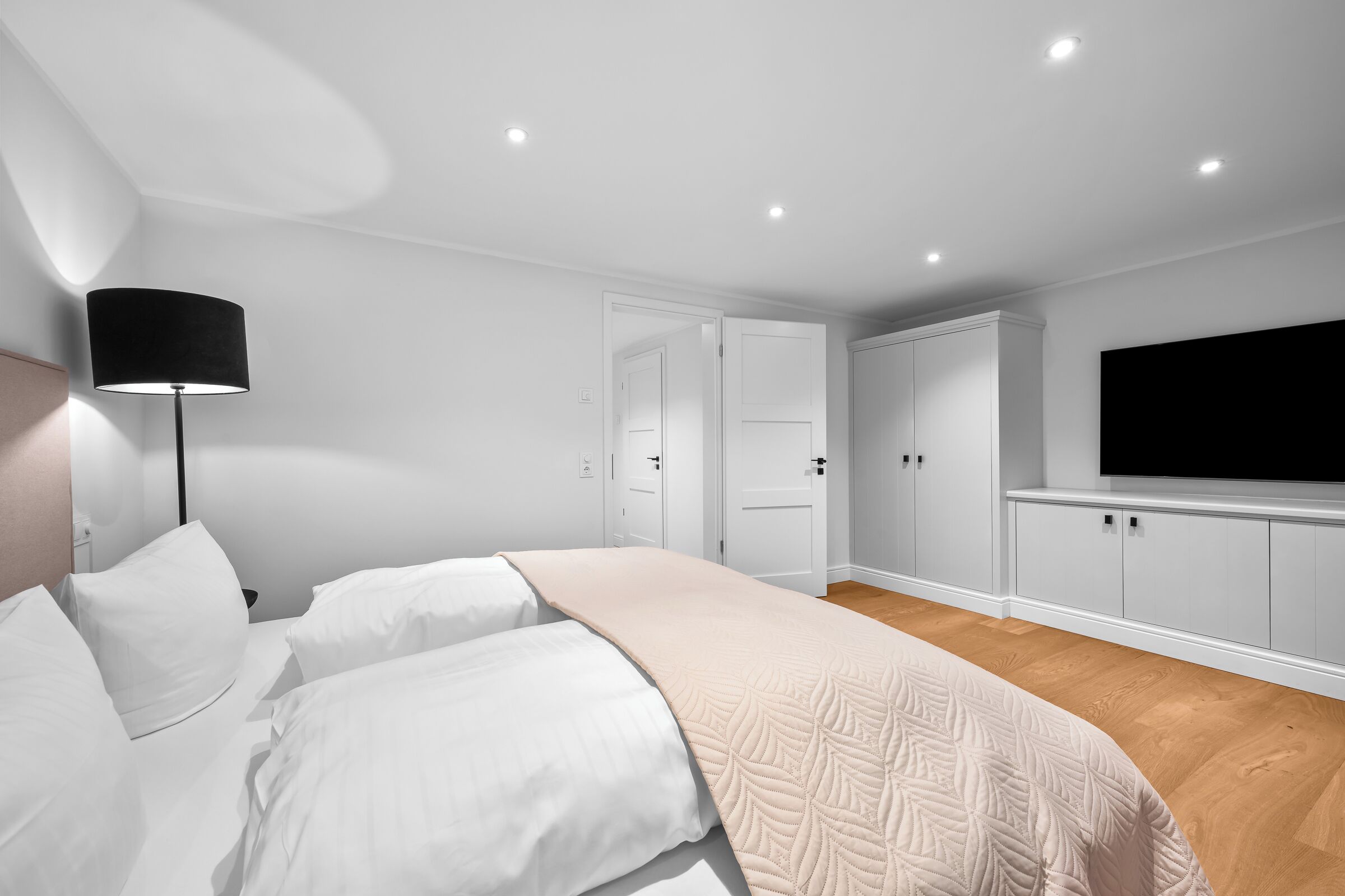 Ein Schlafzimmer mit einem Bett, einer Nachttischlampe, einem Kleiderschrank und einem an der Wand befestigten Fernseher.