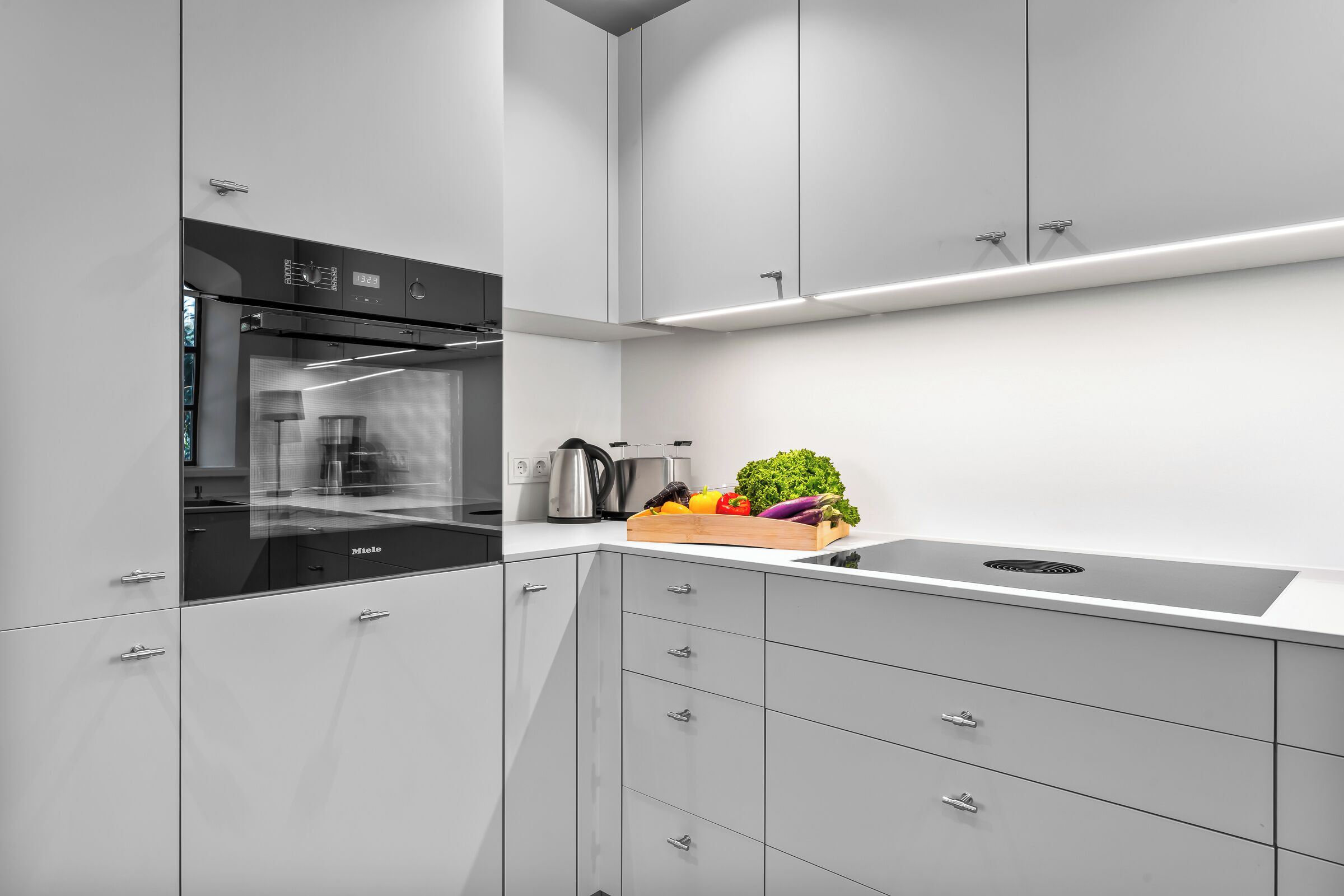 Eine moderne Küche mit weißen Schränken, einem eingebauten Backofen und einer Arbeitsplatte mit frischem Gemüse.