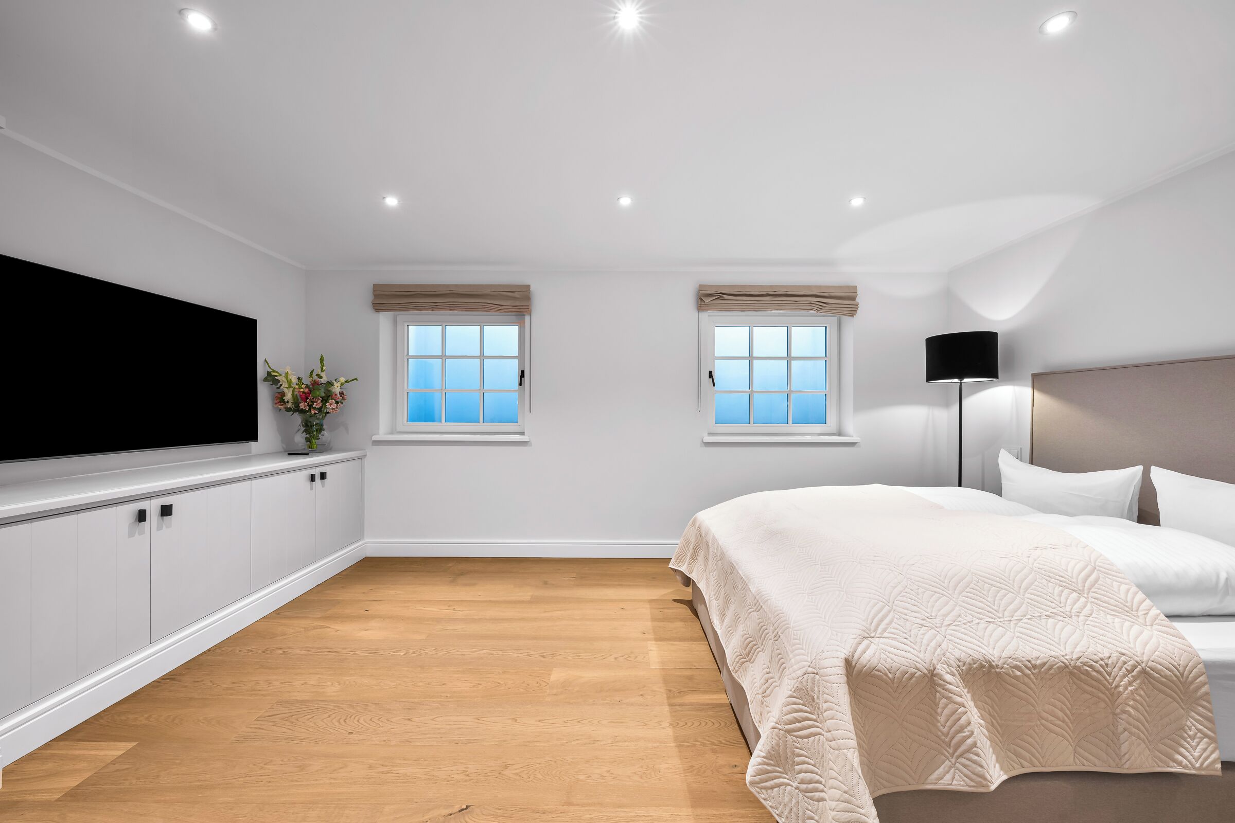 A bedroom with a bed, two windows, a TV, and a plant.