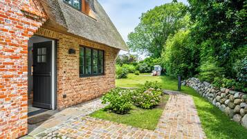 A brick house with a thatched roof, a paved garden pathway, and a stone wall.