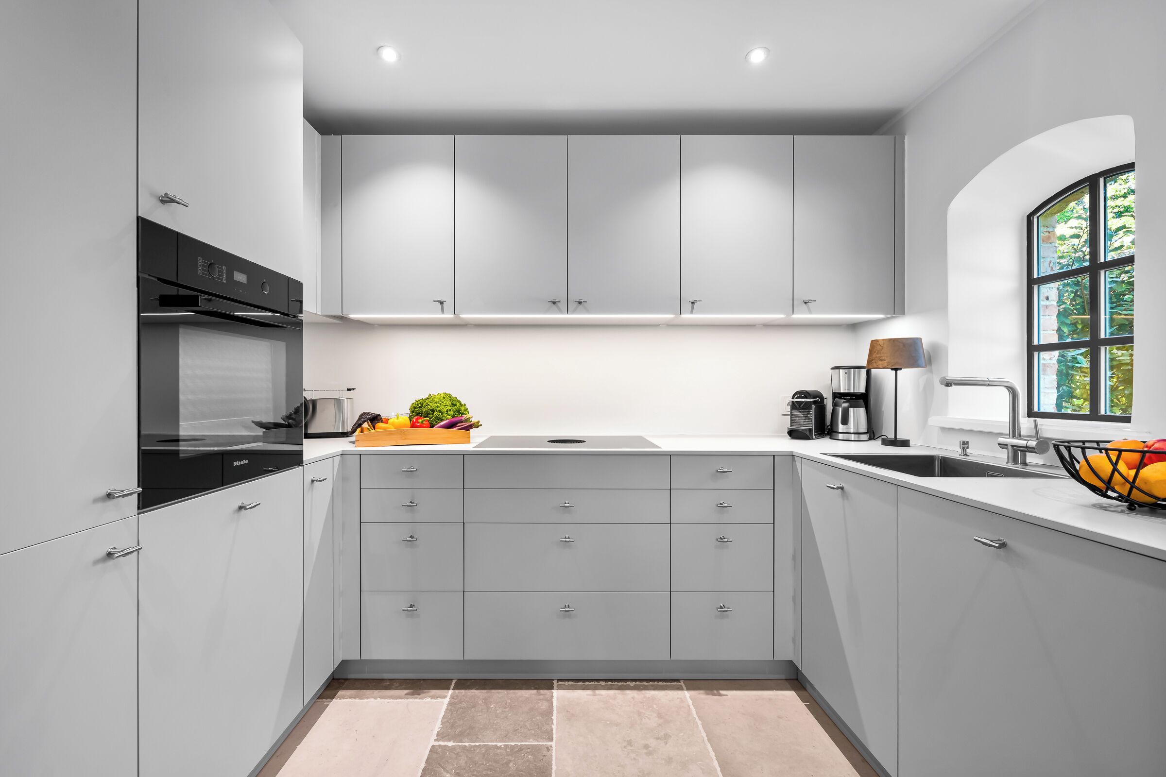 A modern kitchen with grey cabinets, a built-in oven, and a window with a view.