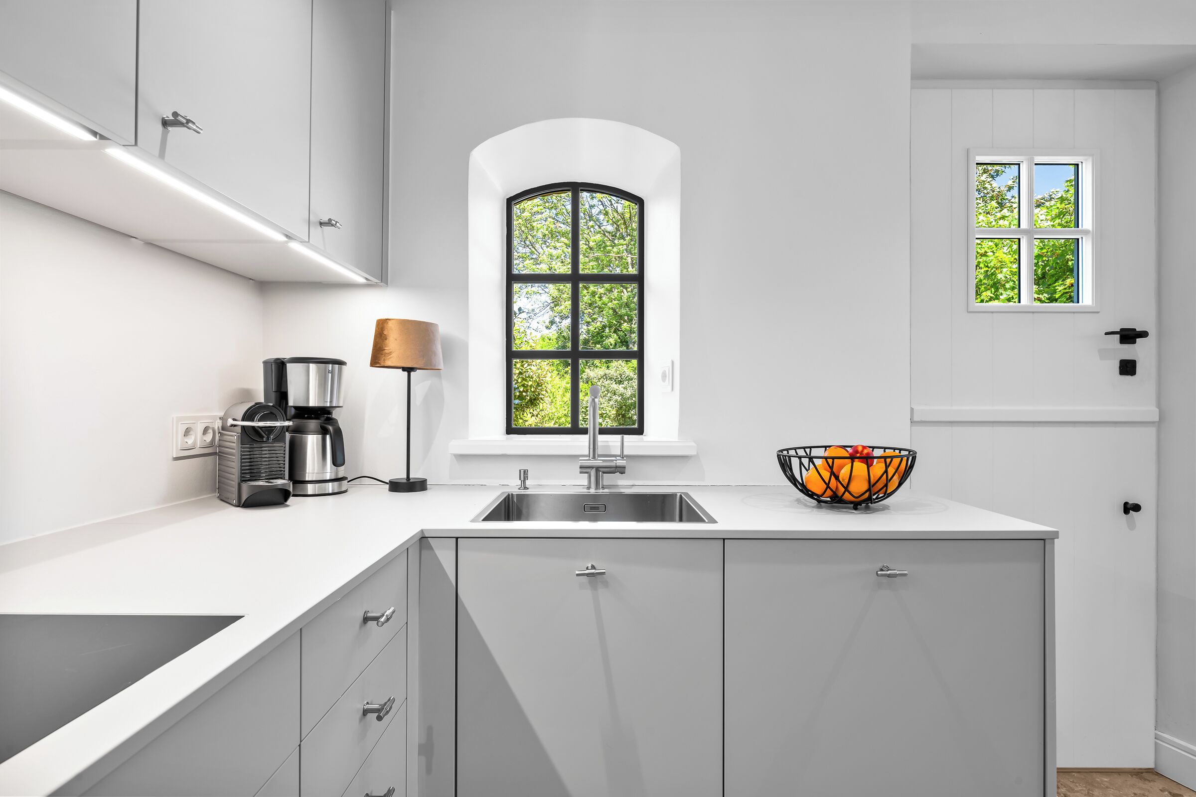 Eine moderne Küche mit integriertem Spülbecken, einer Kaffeemaschine und einem Fenster mit Blick auf Grünflächen.