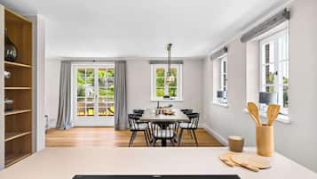 Et moderne spiseområde med et bord dækket til seks personer, et træskab og udsigt til grønne omgivelser.