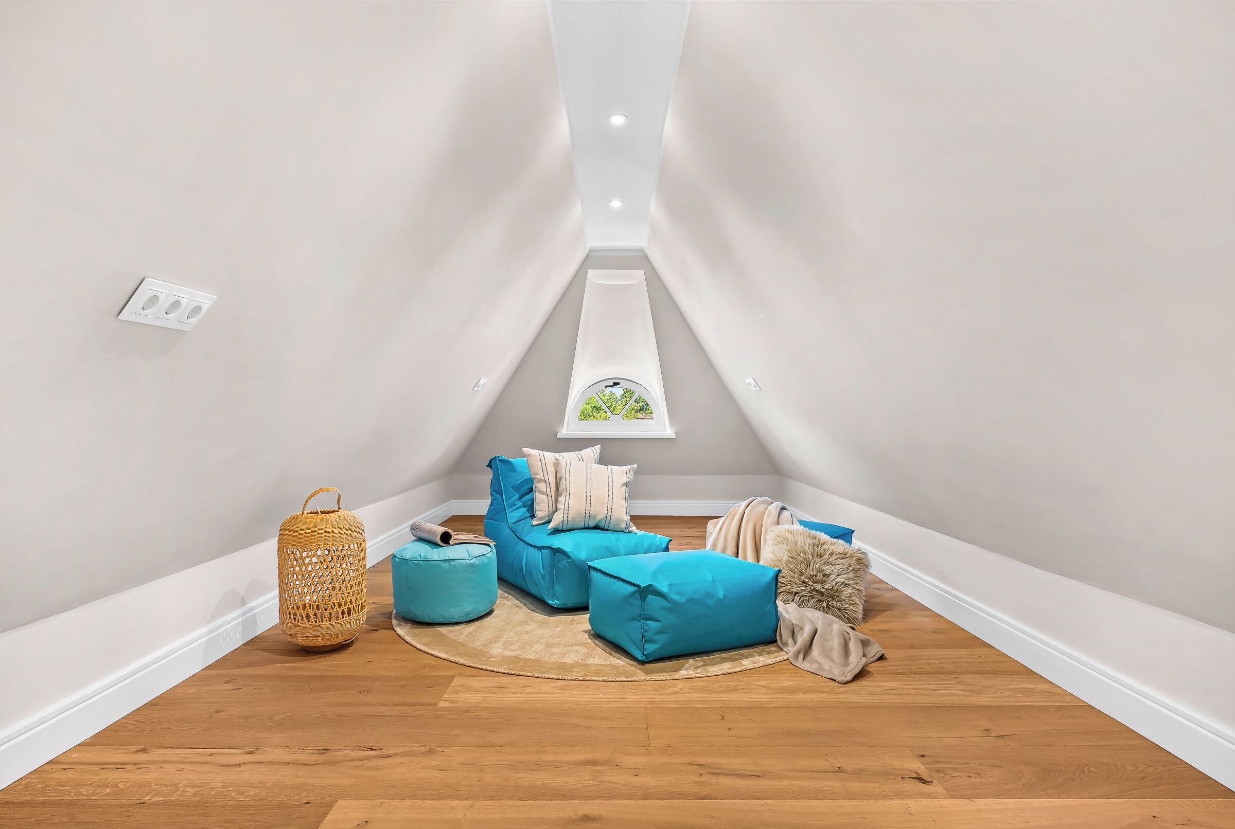 A cozy attic room with a sloped ceiling, a wooden floor, and a small window with a view of greenery.
