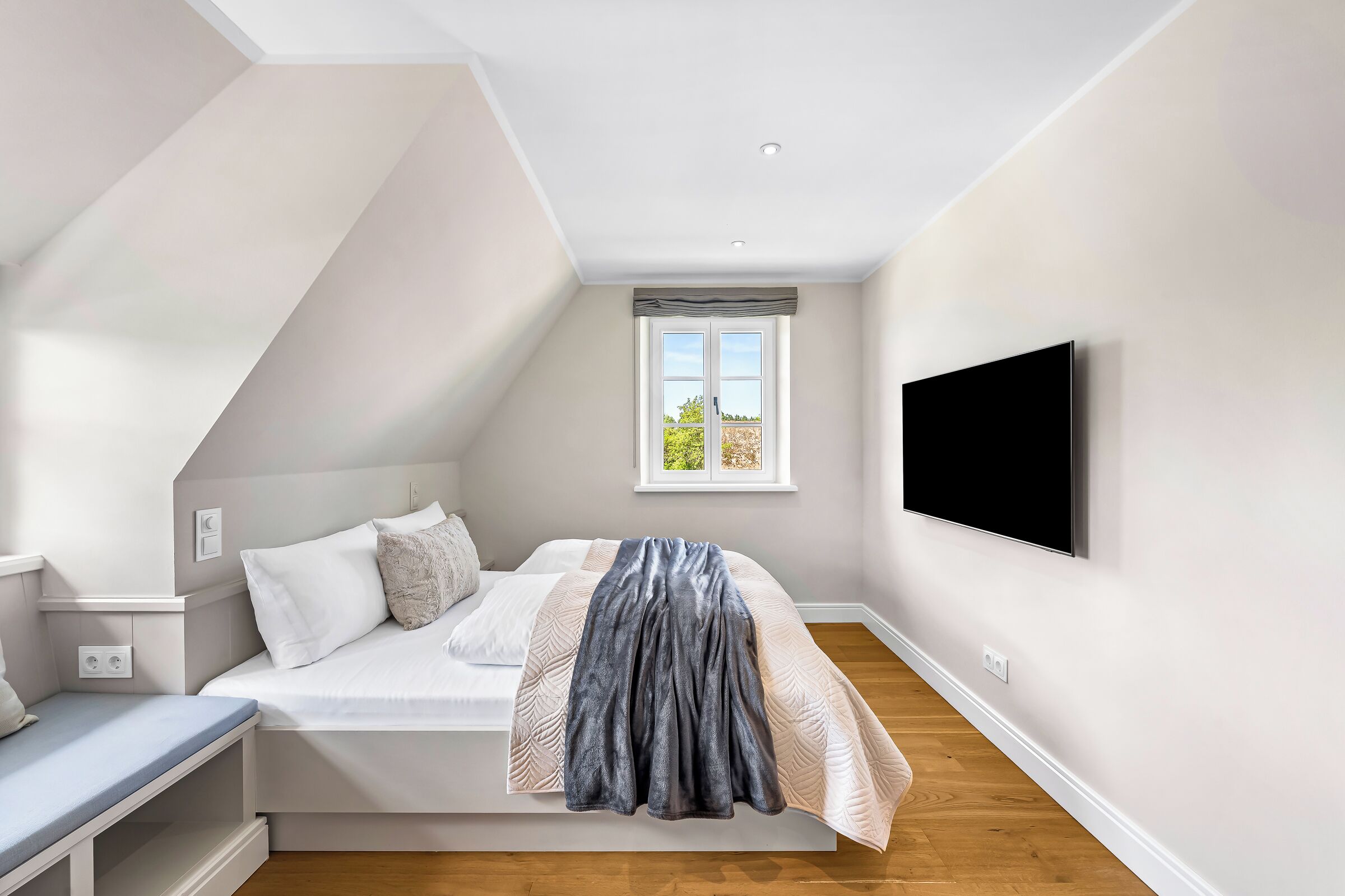 Ein Schlafzimmer mit Bett, einem an der Wand montierten Fernseher, einem Fenster mit Ausblick und einer eingebauten Sitzbank.
