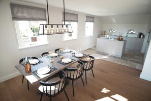 A dining area with a long table, chairs, and a hanging light fixture. - Bontje Hus Archsum on Sylt: Luxury vacation home with sauna and garden (Sylt)