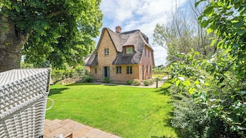 Ein traditionelles Haus mit einem strohgedeckten Dach, umgeben von einem gepflegten Rasen und üppiger Bepflanzung.
