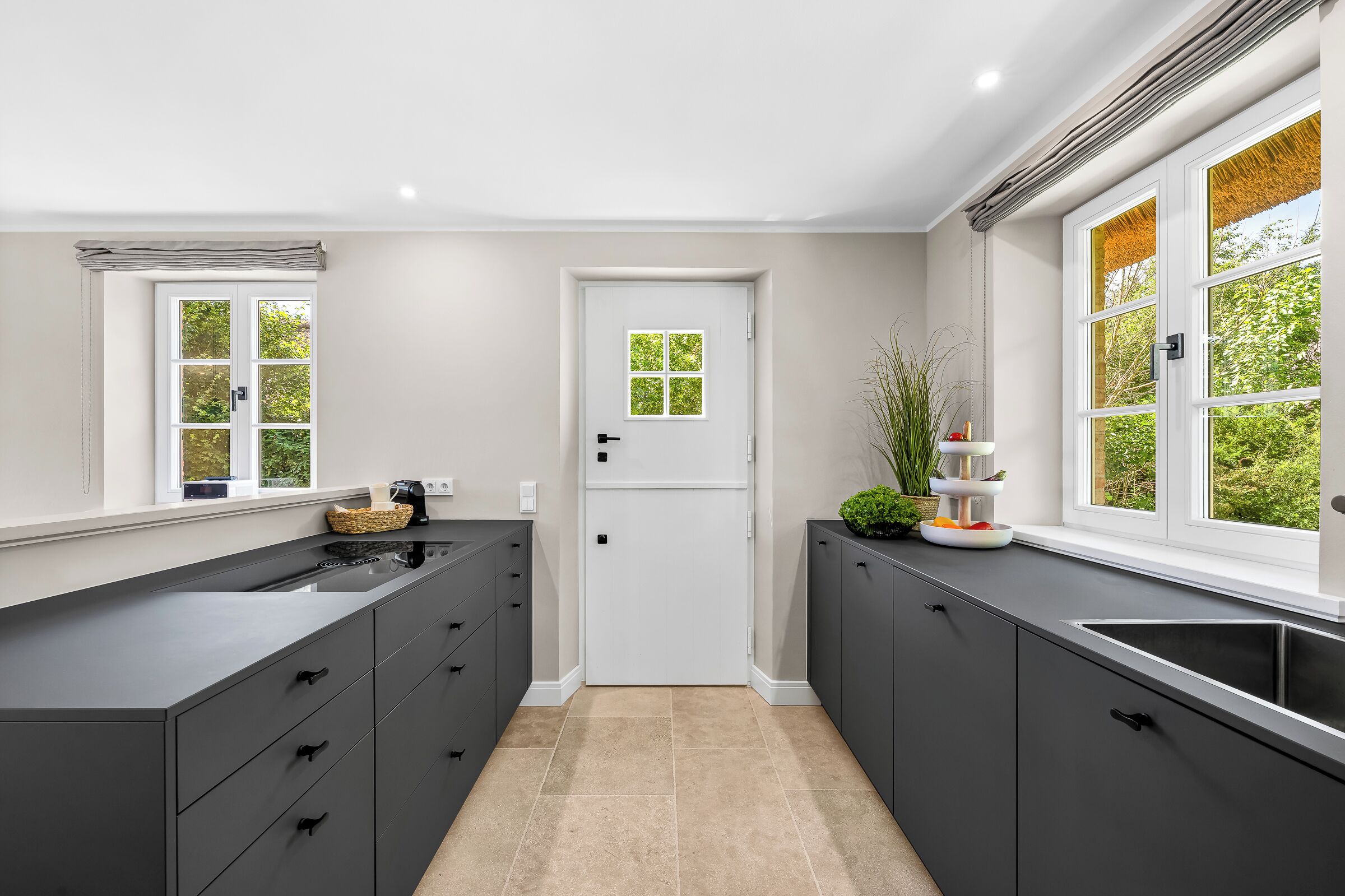 A modern kitchen with dark cabinets, a double sink, and a window with a view of greenery.