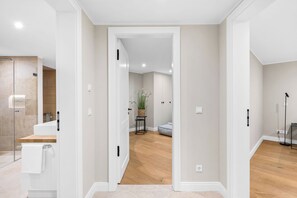 A modern interior with a hallway leading to a bathroom, a seating area, and a plant.