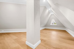 Ein Zimmer mit geneigter Decke, Holzboden und einem kleinen Fenster mit Blick.