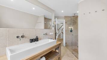 A modern bathroom with a large white sink, a wooden vanity, a mirror, and a glass-enclosed shower.
