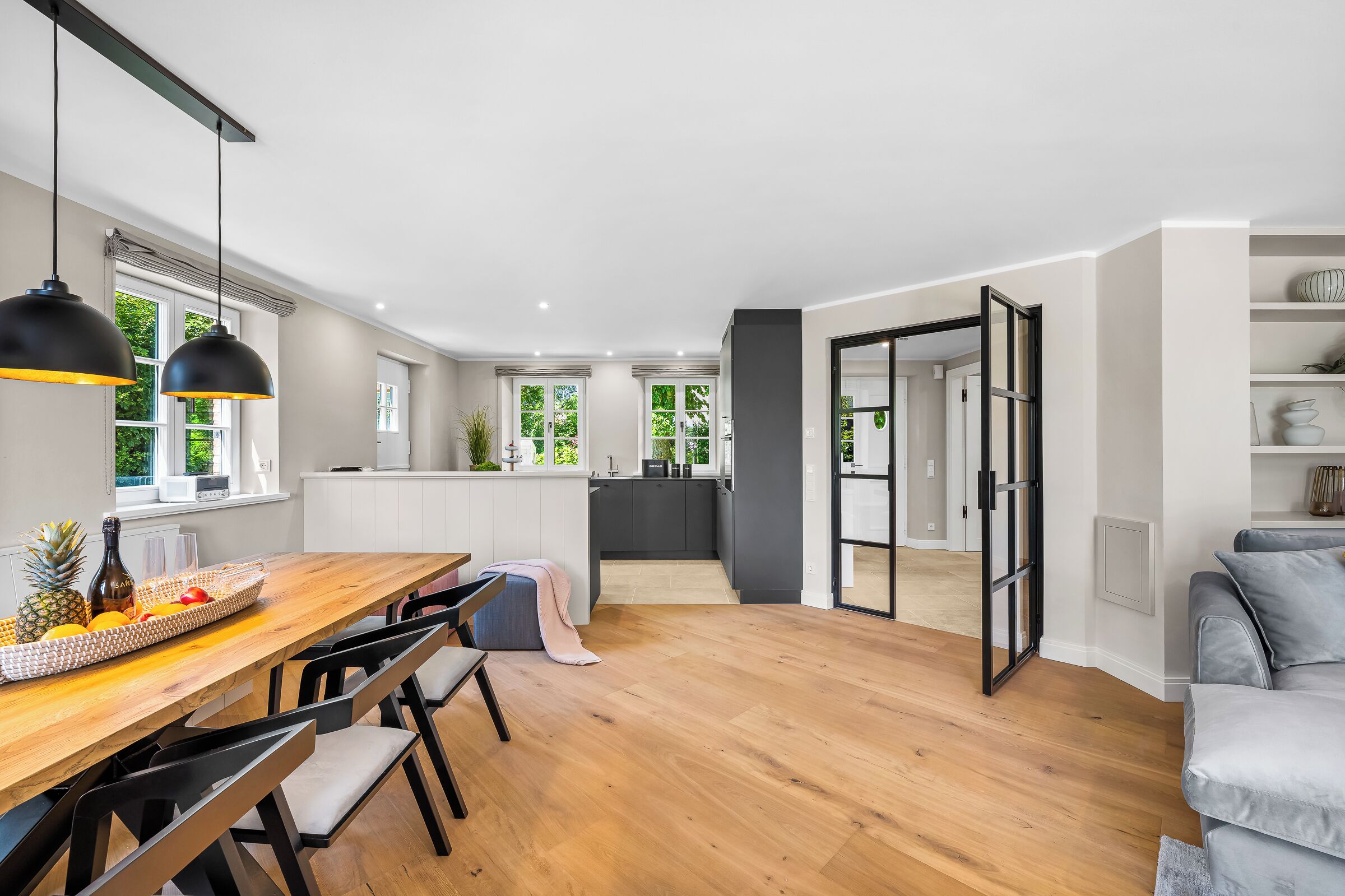 A modern kitchen with a wooden dining table, black chairs, and pendant lights.
