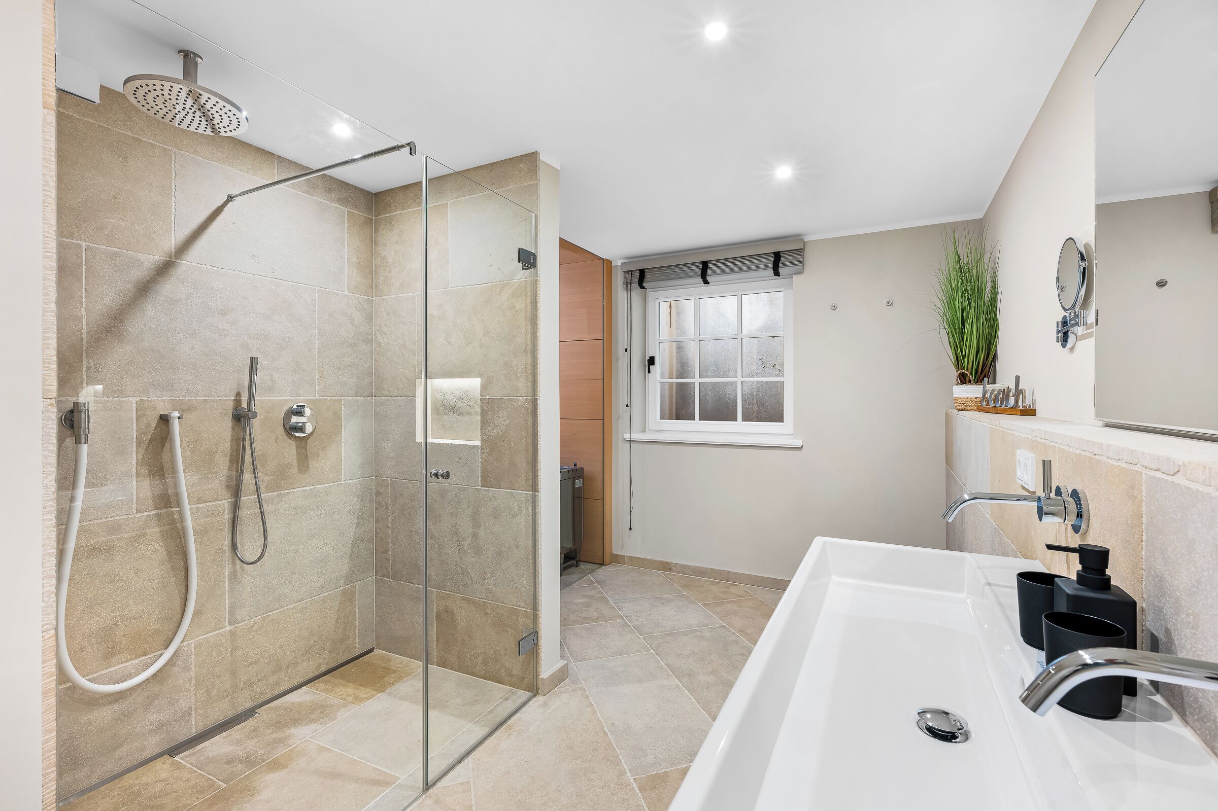 Ein modernes Badezimmer mit einer gläsernen Duschkabine, einer großzügigen Badewanne und einem Fenster für natürliches Licht.