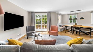 Uma sala de estar moderna com uma televisão de tela plana, um sofá, uma mesa de centro e uma área de jantar com mesa e cadeiras.