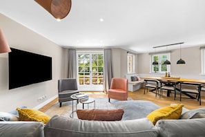 Ein modernes Wohnzimmer mit Flachbildfernseher, einer Couch, einem Couchtisch und einem Essbereich mit Tisch und Stühlen.