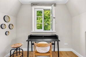 A room with a piano, a window with a view of greenery, and a wall with circular decorations. - Dröm Hus Archsum on Sylt - luxurious vacation home with sauna and 160 m² (Sylt)