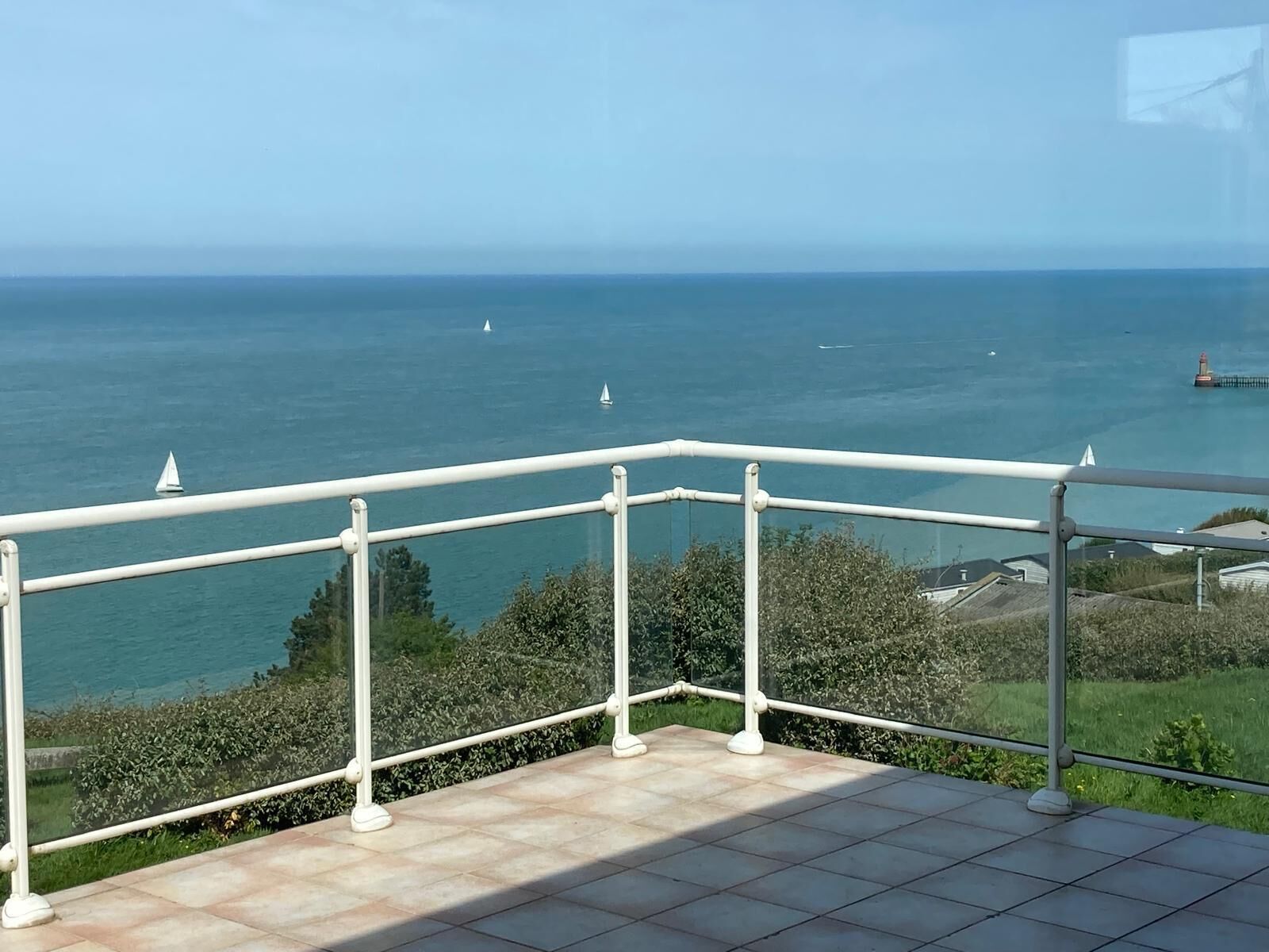 Un balcón con vista al mar, un faro y una zona verde.