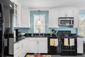 A kitchen with white cabinets, a black stove, a microwave, and a window with blinds. - Lake View Drive House (Bethany Beach)