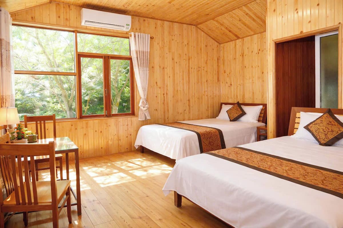 Une pièce de cabane en bois comprenant deux lits, une table, des chaises et une fenêtre avec des rideaux.