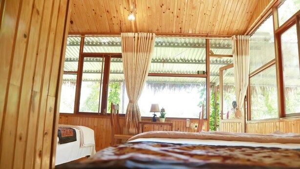 Una habitación de madera con una cama, un escritorio y ventanas amplias.