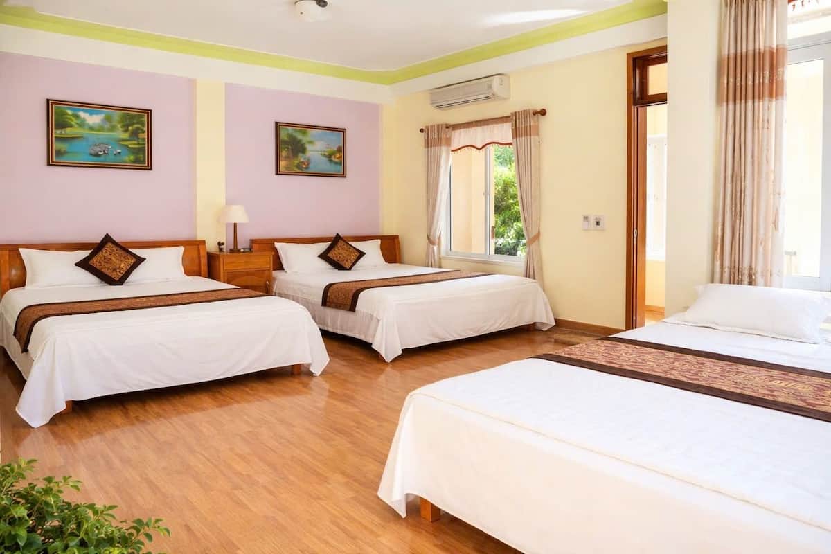 Une chambre d’hôtel avec deux lits simples, un grand lit, un plancher en bois, une fenêtre avec des rideaux et deux climatiseurs fixés au mur.