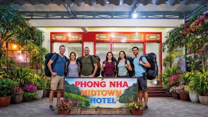 Un grupo de personas frente al cartel del Phong Nha Midtown Hotel, rodeado de plantas en macetas y un acceso cubierto.