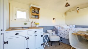 A compact, well-lit room with a kitchenette, a bed with patterned bedding, a small white chair, and a wooden table. - A lodge/cabin that sleeps 2 guests  in 1 bedroom - 3 nights for the price of 2 nights in July! (Ringwood)