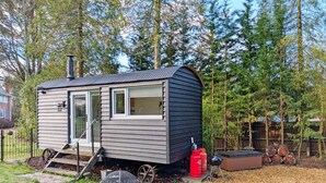 A small cabin with a sliding door, a fire pit, and a hot tub in a wooded area. - A lodge/cabin that sleeps 2 guests  in 1 bedroom - 3 nights for the price of 2 nights in July! (Ringwood)