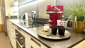 Uma cozinha moderna com uma cafeteira vermelha, fogão vitrocerâmico e um vaso de planta.