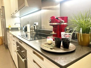 Eine moderne Küche mit einer roten Kaffeemaschine, einem Glaskeramikkochfeld und einem Blumentopf.