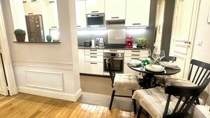 Cozinha compacta com armários brancos, micro-ondas, torradeira e área de refeições com mesa e cadeiras.