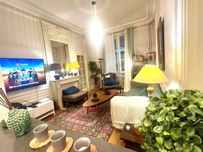 Ein Wohnzimmer mit Fernseher, Sofa, Ohrensessel, Couchtisch und Zierpflanzen.