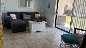 Un salon comprenant un canapé, une table basse, un fauteuil et une porte-fenêtre coulissante donnant sur un espace extérieur.