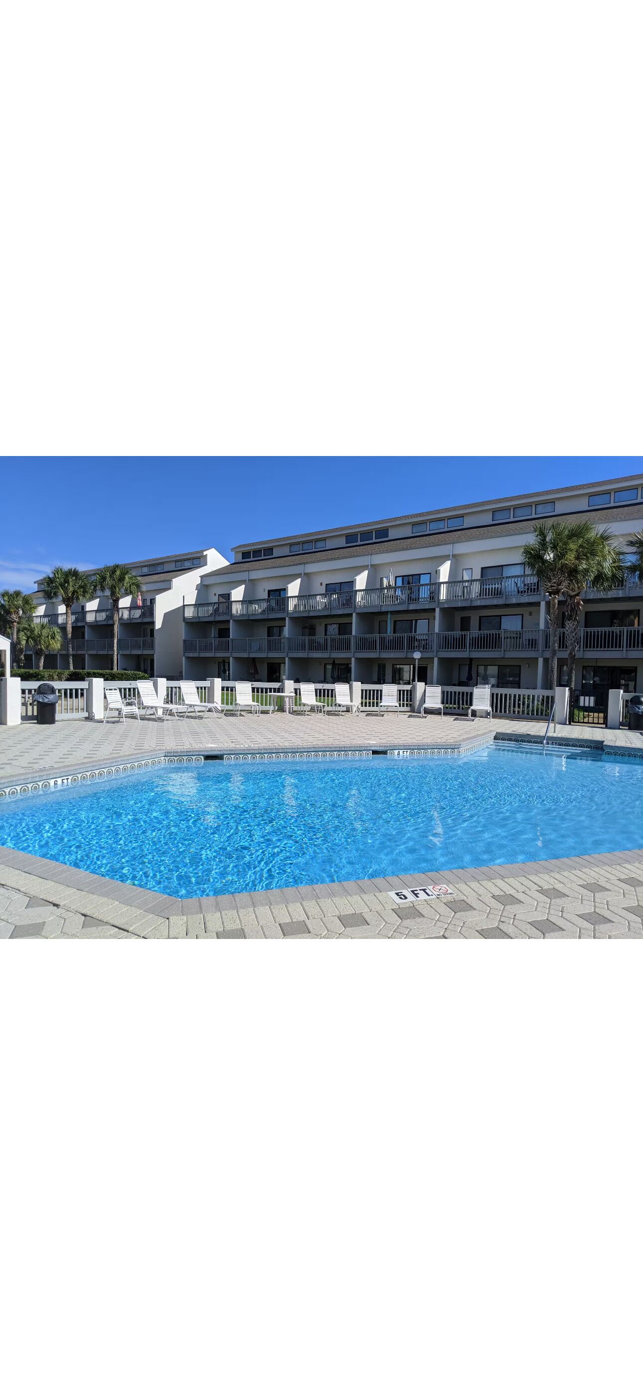 A swimming pool with a tiled deck, a building with multiple balconies, and palm trees.