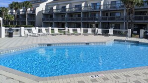 Une piscine avec une terrasse carrelée, un bâtiment doté de nombreux balcons et des palmiers.