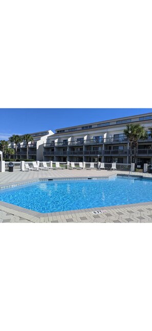 A swimming pool with a tiled deck, a building with multiple balconies, and palm trees. - Welcome to Margaritaville, Where it’s always 5 o’clock! Steps from the beach! (Panama City Beach)