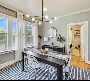 A dining area with a dark wooden table, white chairs, a striped rug, and a modern chandelier.