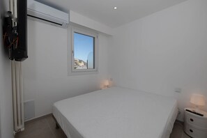 Ein Schlafzimmer mit Bett, Fenster, Heizkörper und einem an der Wand befestigten Fernseher.