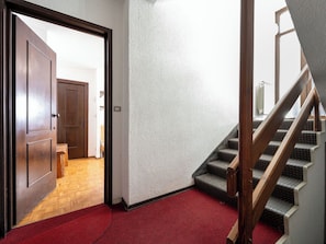 Ein Flur mit einer Holztür, einem roten Teppich, einer Treppe mit einem hölzernen Geländer und einer strukturierten Wand.