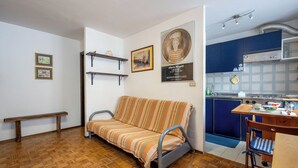 Ein gemütlicher Wohnraum mit Sofa, Sitzbank, kleinem Tisch und Küchenzeile.