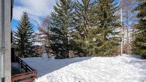 Schneebedeckte Landschaft mit einer hölzernen Bank, Schneemännern und immergrünen Bäumen.
