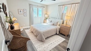 Ein Schlafzimmer mit einem Bett, Nachttischen, einer Lampe, einem Sessel, einem Teppich und einem Fenster mit Vorhängen.