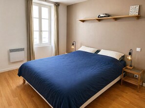 A bedroom with a large bed, a window with curtains, a wall-mounted shelf with a projector, and a bedside table with a lamp. - T2 apartment in the center of Biarritz (Biarritz)