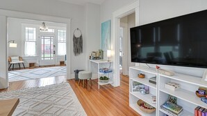 Een woonkamer met een grote televisie, houten vloeren en witte muren.