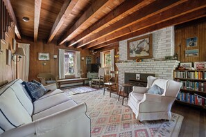 Un salón acogedor con chimenea, vigas de madera, una estantería y asientos cómodos.