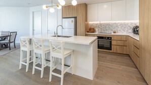 Eine moderne Küche mit einer zentralen Kochinsel, weißen Barhocker, einem Einbauofen und Holzschränken.